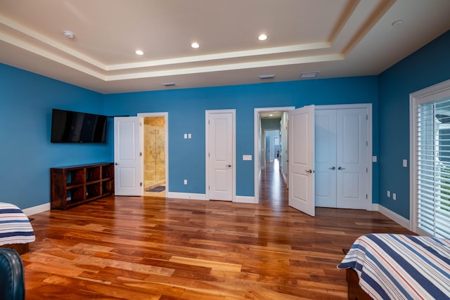 bedroom with connected bathroom, dark hardwood / wood-style floors, and a raised ceiling