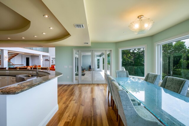 dining room featuring sink, a tray ceiling, french doors, and light wood-type flooring