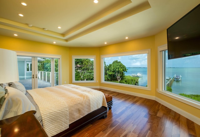 bedroom featuring a tray ceiling, dark wood-type flooring, access to exterior, and french doors