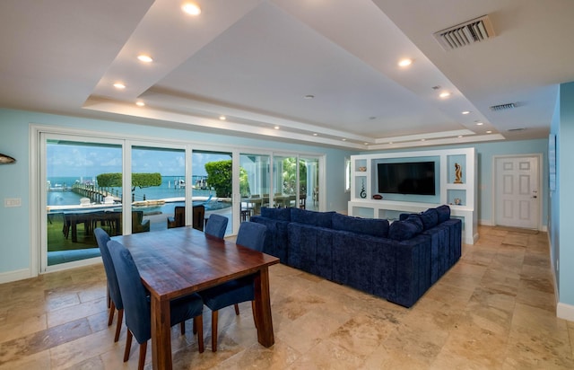 living room featuring a tray ceiling, a healthy amount of sunlight, and a water view