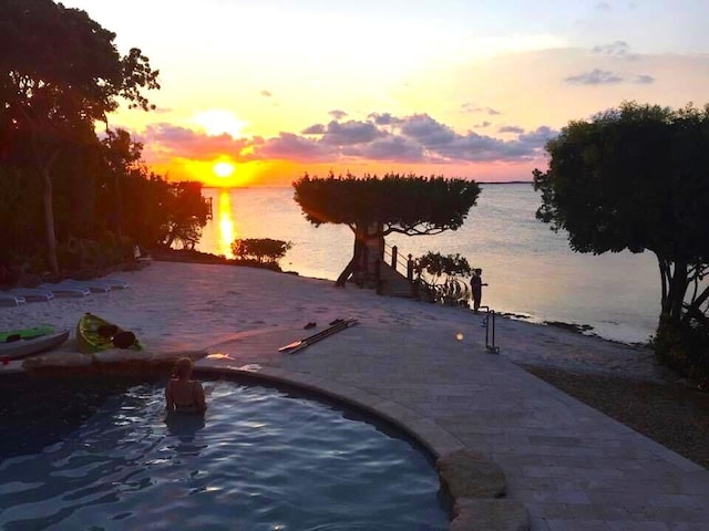 pool at dusk with a water view and a patio area