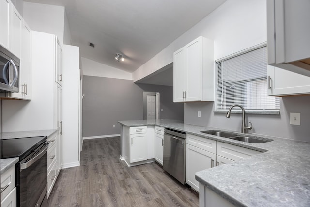 kitchen featuring appliances with stainless steel finishes, white cabinets, vaulted ceiling, a sink, and a peninsula