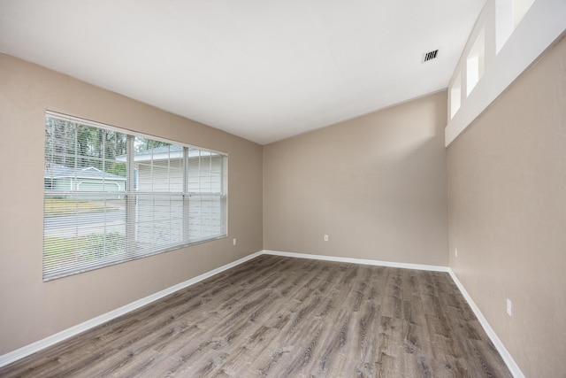 empty room with wood finished floors, visible vents, and baseboards