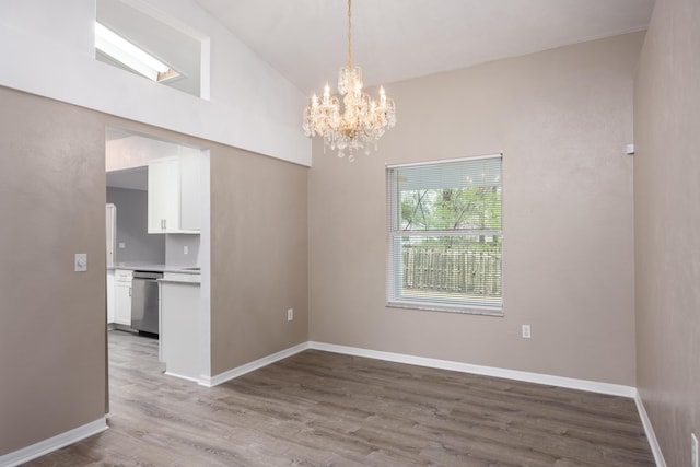 empty room with lofted ceiling, an inviting chandelier, baseboards, and wood finished floors