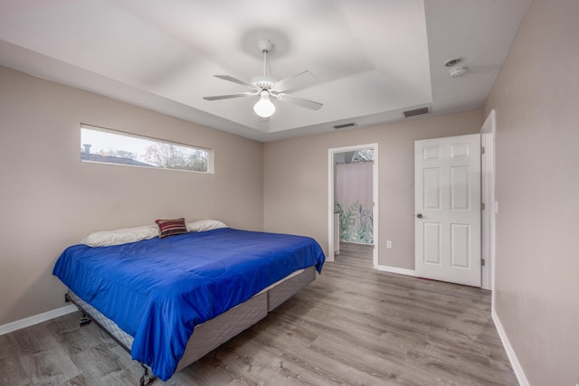 bedroom featuring a tray ceiling, visible vents, baseboards, and wood finished floors