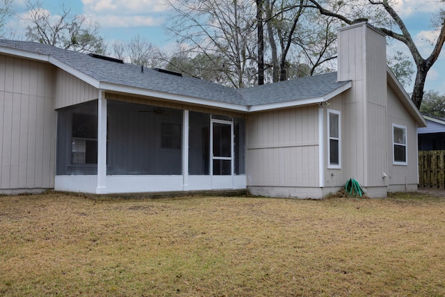 rear view of house featuring a lawn, roof with shingles, a chimney, and a sunroom