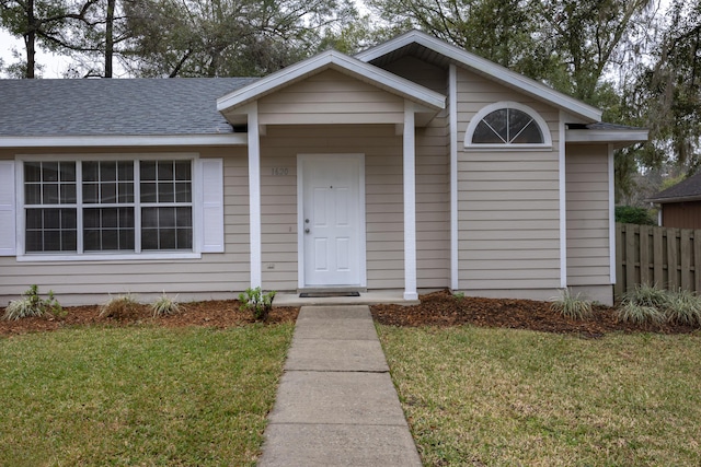 view of front facade with a front lawn, roof with shingles, and fence