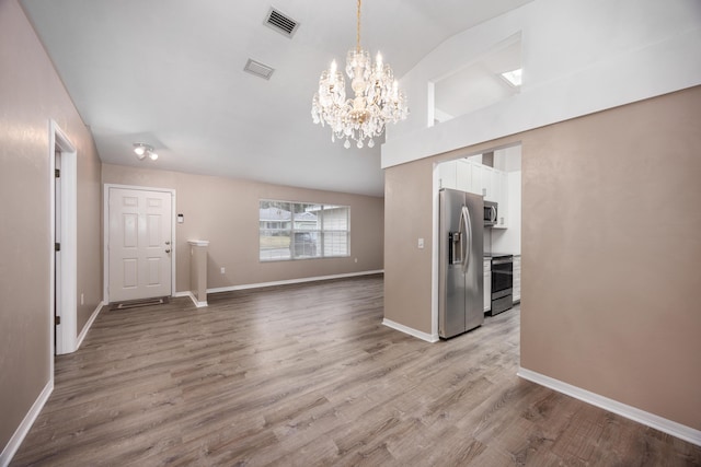 unfurnished living room with baseboards, visible vents, vaulted ceiling, and wood finished floors