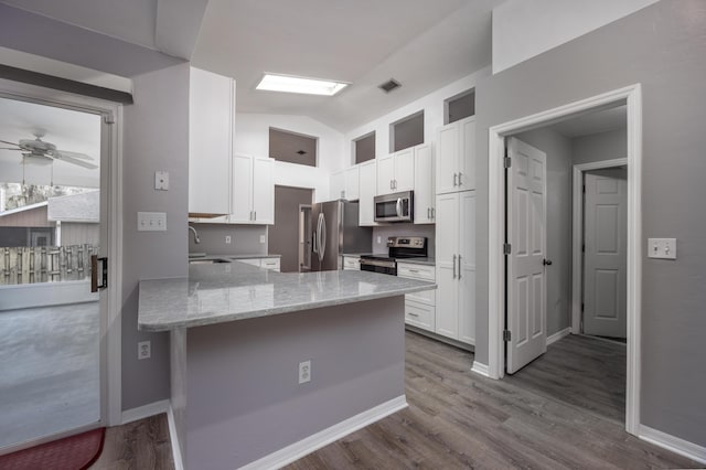 kitchen with appliances with stainless steel finishes, white cabinetry, a sink, light stone countertops, and a peninsula