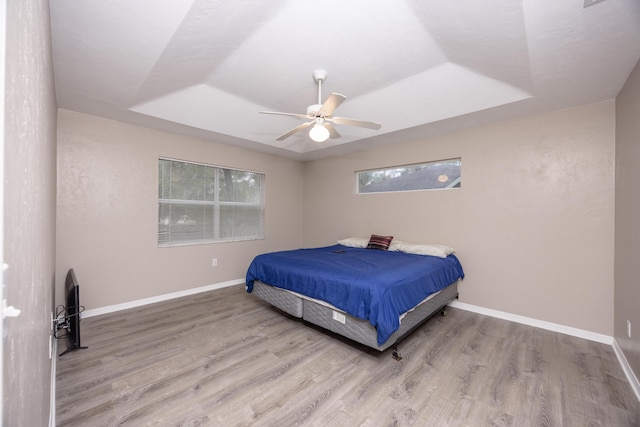 bedroom with baseboards, a tray ceiling, and wood finished floors