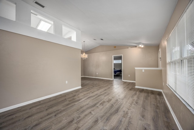 empty room with wood finished floors, visible vents, baseboards, vaulted ceiling, and an inviting chandelier