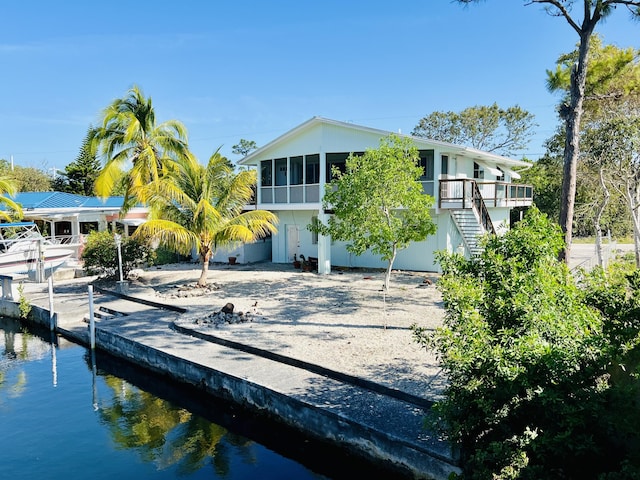 view of front facade featuring a water view, a dock, and a sunroom