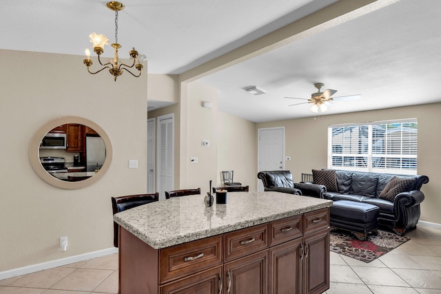 kitchen featuring pendant lighting, light tile patterned floors, stainless steel appliances, a center island, and ceiling fan with notable chandelier