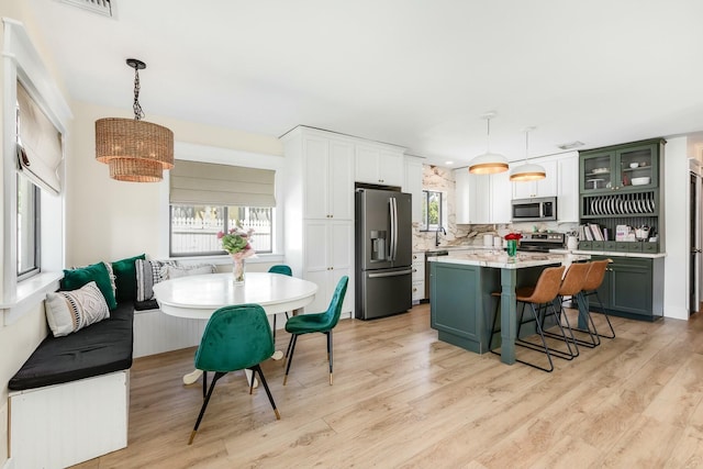 kitchen featuring breakfast area, glass insert cabinets, hanging light fixtures, stainless steel appliances, and light countertops