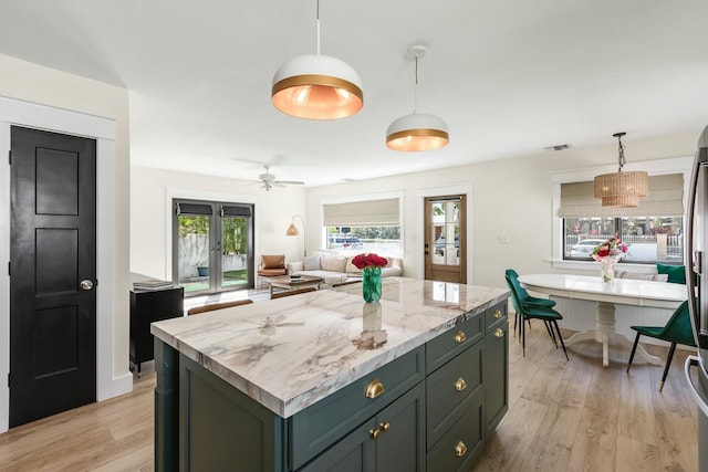 kitchen featuring a center island, french doors, light wood-type flooring, light stone countertops, and decorative light fixtures