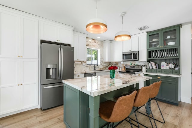 kitchen featuring stainless steel appliances, a kitchen island, visible vents, hanging light fixtures, and glass insert cabinets