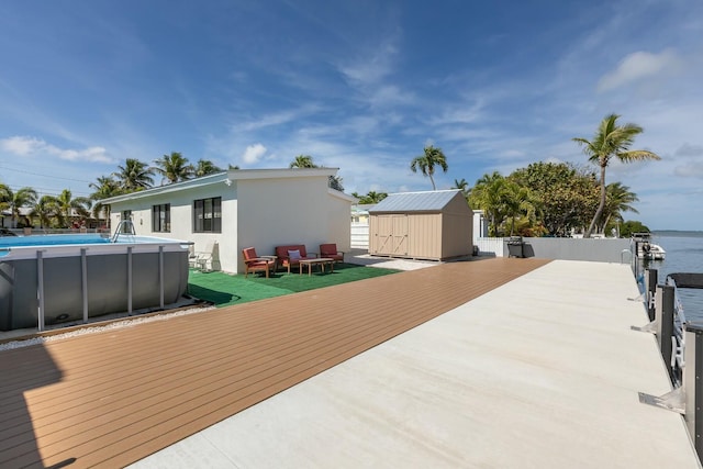 wooden terrace with a water view, a storage shed, an outdoor pool, and an outbuilding