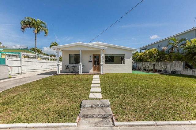 view of front of house featuring covered porch, a front lawn, fence, and stucco siding