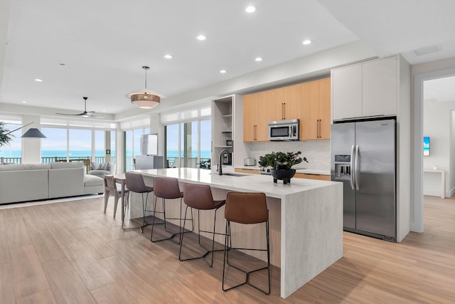 kitchen with stainless steel appliances, a water view, open floor plan, hanging light fixtures, and an island with sink