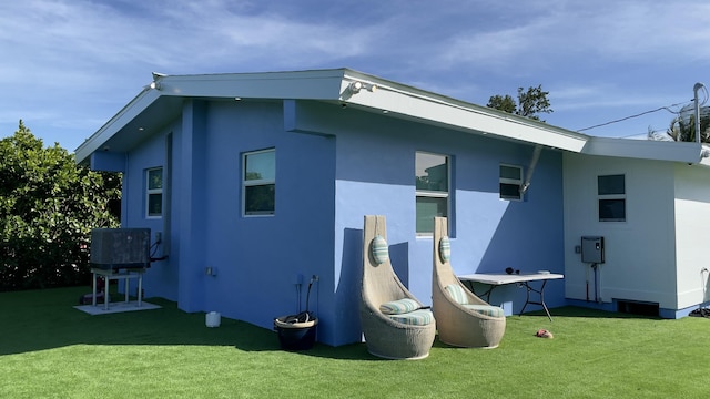 rear view of house featuring central AC unit and a lawn