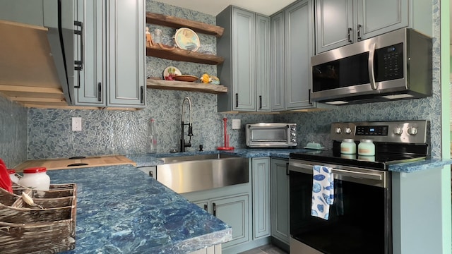 kitchen featuring sink, gray cabinets, appliances with stainless steel finishes, tasteful backsplash, and dark stone counters