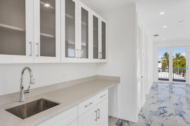 kitchen with light stone countertops, sink, and white cabinets