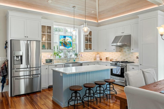 kitchen with sink, decorative light fixtures, appliances with stainless steel finishes, a kitchen island, and wall chimney range hood