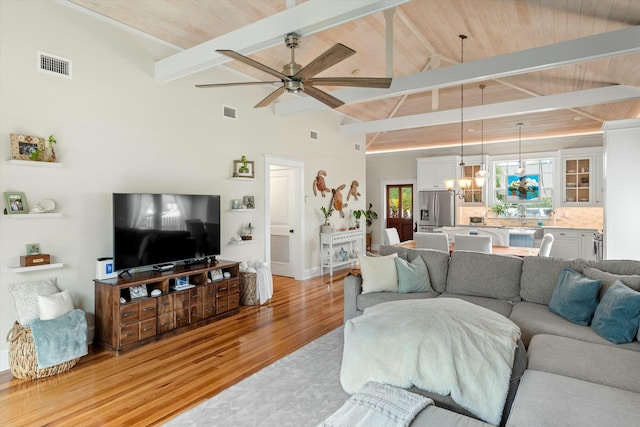 living room featuring ceiling fan with notable chandelier, light hardwood / wood-style flooring, high vaulted ceiling, and beamed ceiling