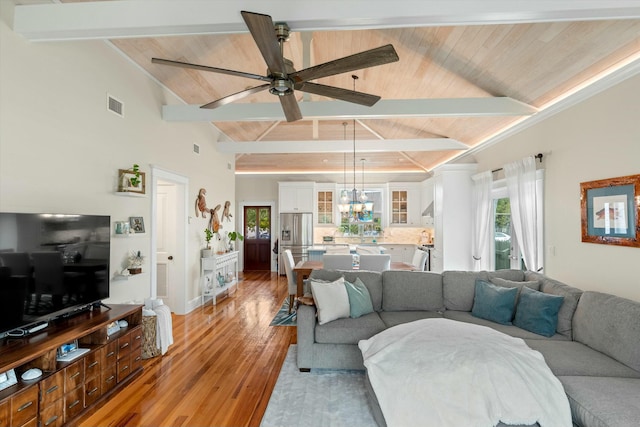 living room with ceiling fan with notable chandelier, wooden ceiling, light wood-type flooring, and vaulted ceiling with beams