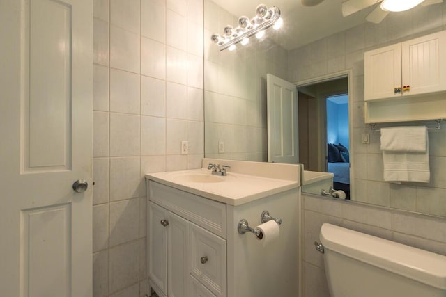 bathroom featuring vanity, tile walls, ceiling fan, and toilet