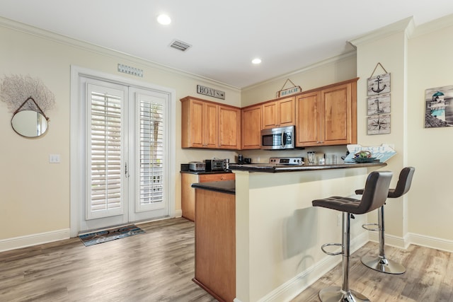 kitchen with crown molding, light hardwood / wood-style flooring, kitchen peninsula, and a breakfast bar