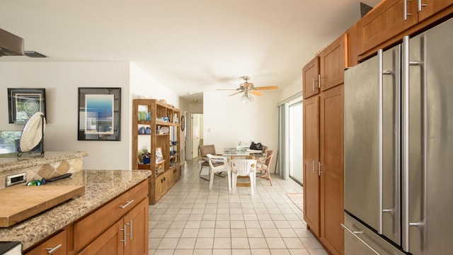 kitchen featuring light tile patterned floors, high quality fridge, ceiling fan, and light stone countertops