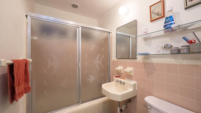 full bathroom featuring bath / shower combo with glass door, toilet, sink, and tile walls