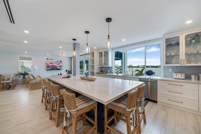 kitchen featuring a breakfast bar area, hanging light fixtures, dishwasher, a kitchen island, and white cabinets