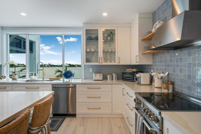 kitchen featuring sink, white cabinets, light stone counters, stainless steel appliances, and wall chimney range hood