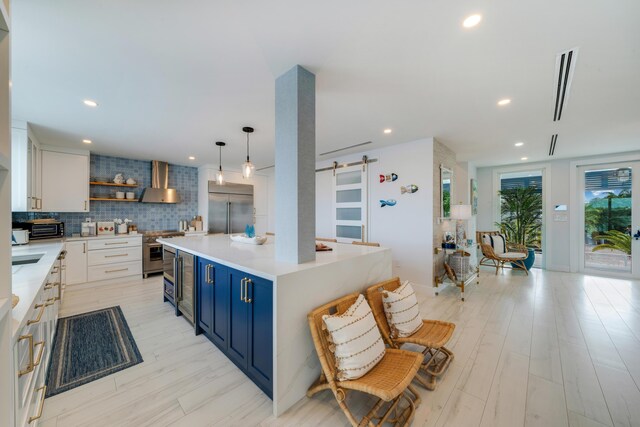 kitchen featuring premium appliances, white cabinets, blue cabinets, a barn door, and wall chimney exhaust hood