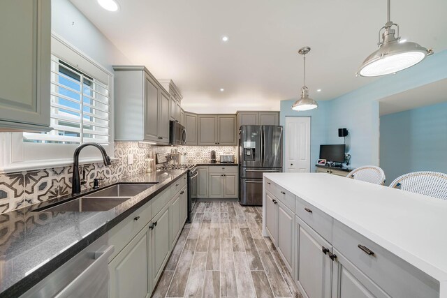 kitchen with sink, gray cabinetry, hanging light fixtures, appliances with stainless steel finishes, and decorative backsplash