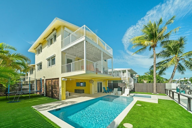 back of house featuring a patio, a balcony, a trampoline, a swimming pool with hot tub, and a yard