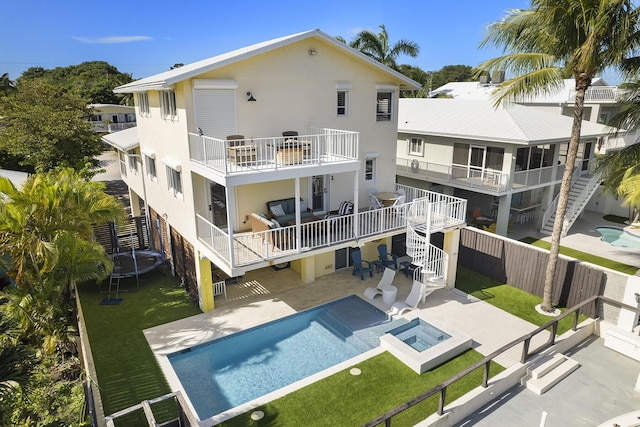 rear view of property featuring a patio area, a balcony, a trampoline, a lawn, and a pool with hot tub