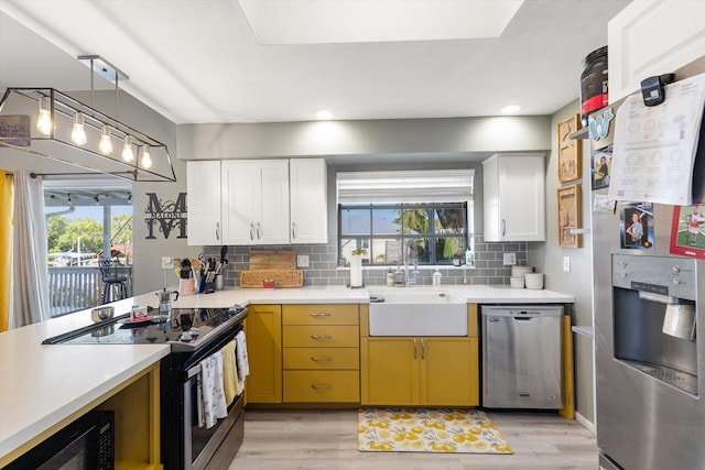 kitchen featuring sink, hanging light fixtures, appliances with stainless steel finishes, white cabinets, and backsplash