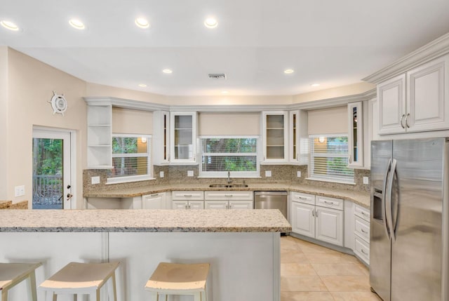 kitchen featuring sink, stainless steel appliances, light stone countertops, white cabinets, and a kitchen bar