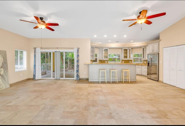 kitchen featuring stainless steel fridge, a breakfast bar area, ceiling fan, light stone countertops, and kitchen peninsula