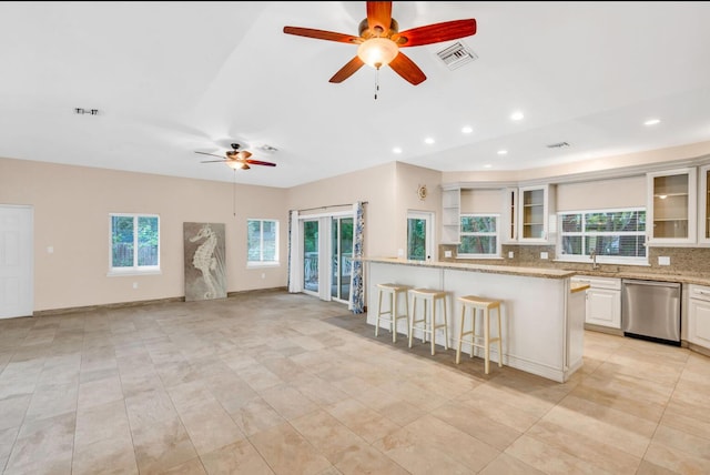 kitchen featuring a breakfast bar, tasteful backsplash, stainless steel dishwasher, light stone countertops, and white cabinets