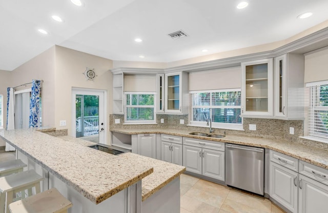 kitchen featuring sink, white cabinets, a kitchen bar, stainless steel dishwasher, and light stone countertops