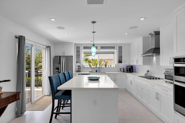 kitchen featuring sink, appliances with stainless steel finishes, white cabinets, a kitchen island, and wall chimney exhaust hood