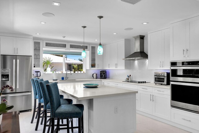 kitchen featuring white cabinets, stainless steel appliances, a center island, and wall chimney range hood