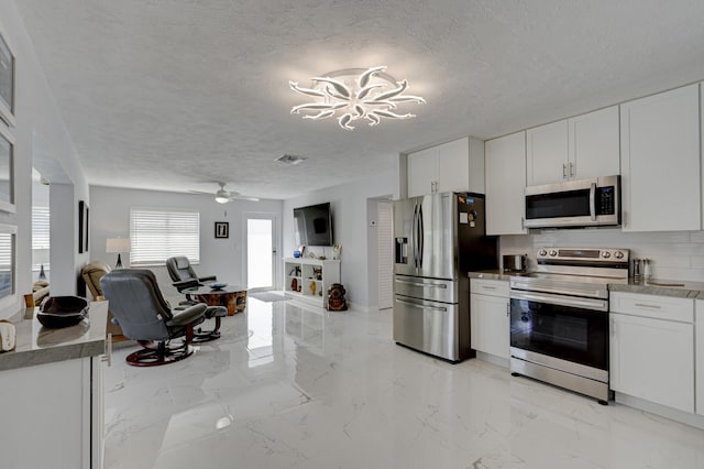 kitchen featuring white cabinetry, a textured ceiling, stainless steel appliances, ceiling fan with notable chandelier, and decorative backsplash