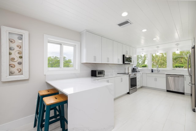 kitchen with stainless steel appliances, white cabinetry, kitchen peninsula, and decorative light fixtures