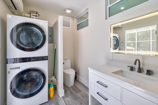 laundry room featuring sink, a wall mounted air conditioner, light wood-type flooring, and stacked washer / dryer