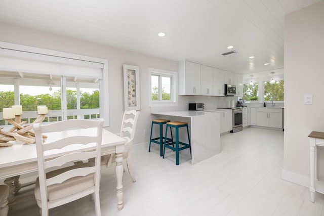 kitchen with a breakfast bar area, tasteful backsplash, kitchen peninsula, stainless steel appliances, and white cabinets